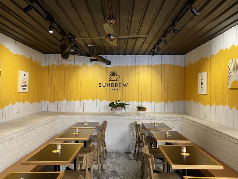Inside Sunbrew Cafe: timber tables beneath a yellow and white painted wall with the Sunbrew logo