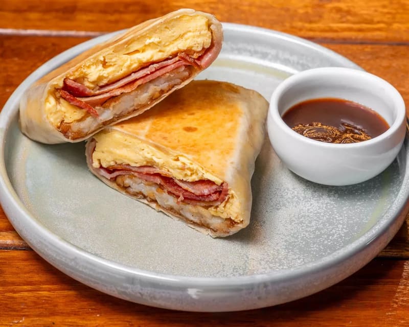Bacon, egg and hash brown wrap cut in half, showing scrambled egg, Streaky Bacon and hash brown, with sauce on the side